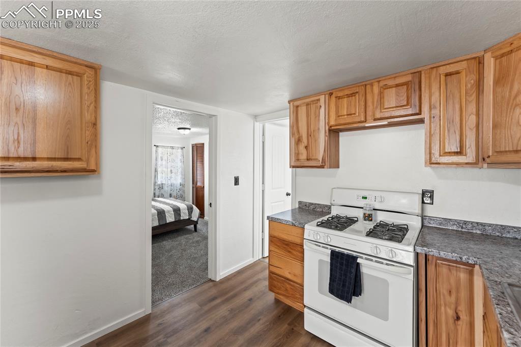 Image 16 of 26: Kitchen featuring white gas range, a textured ceiling, dark wood-style floo