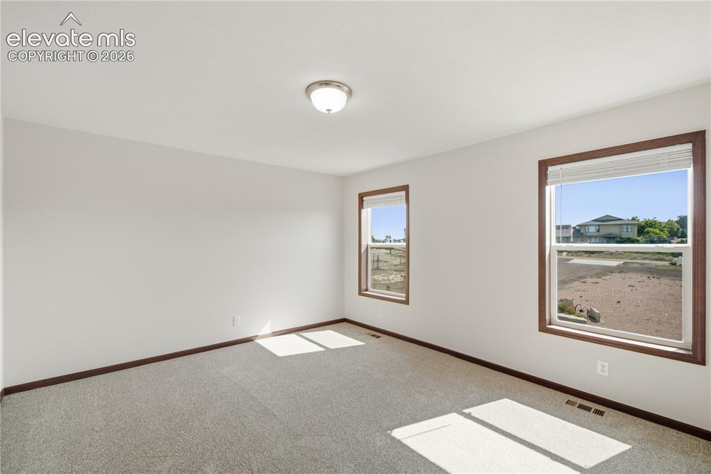 Image 10 of 26: Neutral wall colors, two windows with wood-finish trim, and gray carpeting