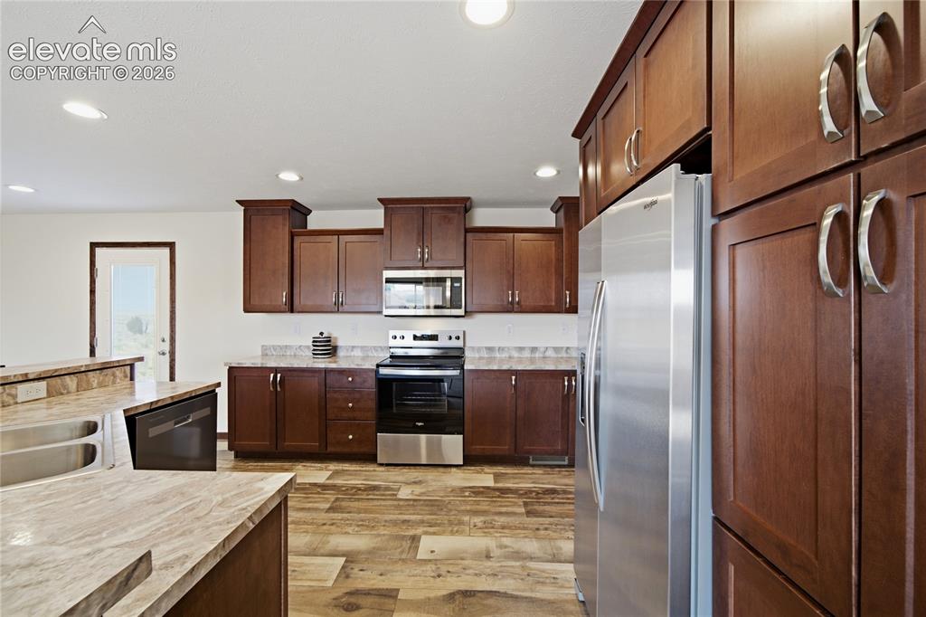 Image 5 of 26: Kitchen featuring wood-finish flooring, dark wood cabinetry, stainless stee