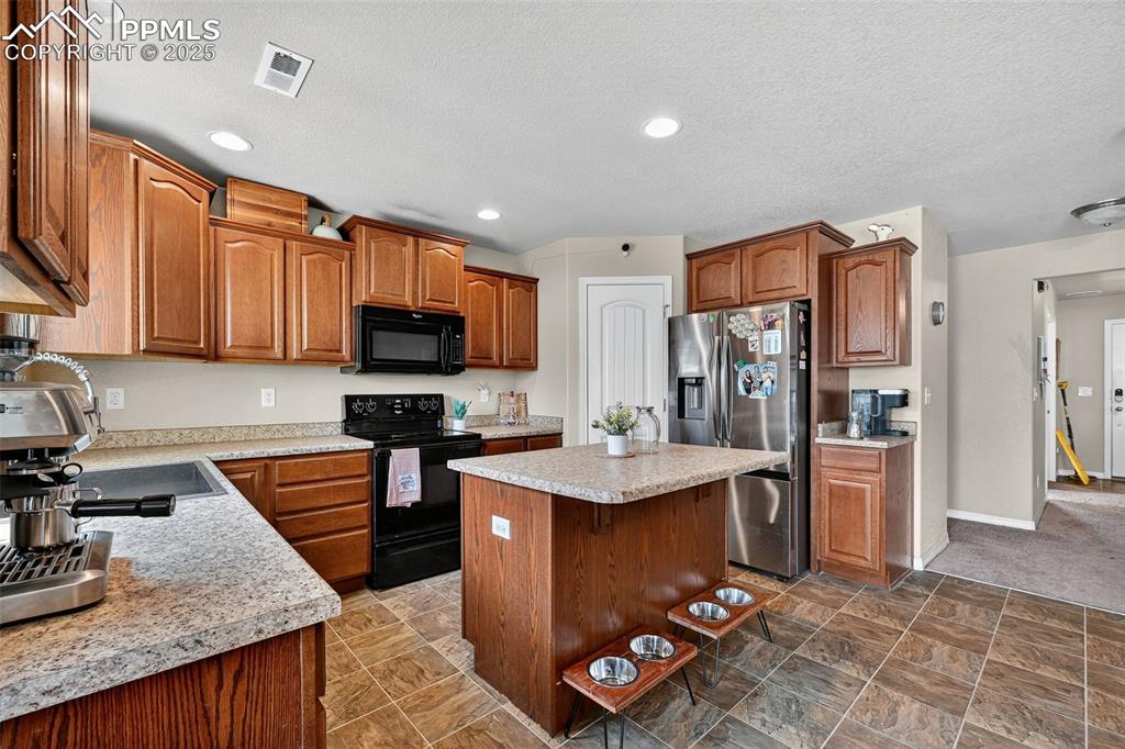 Image 10 of 33: Kitchen featuring black appliances, a kitchen island, a breakfast bar area,