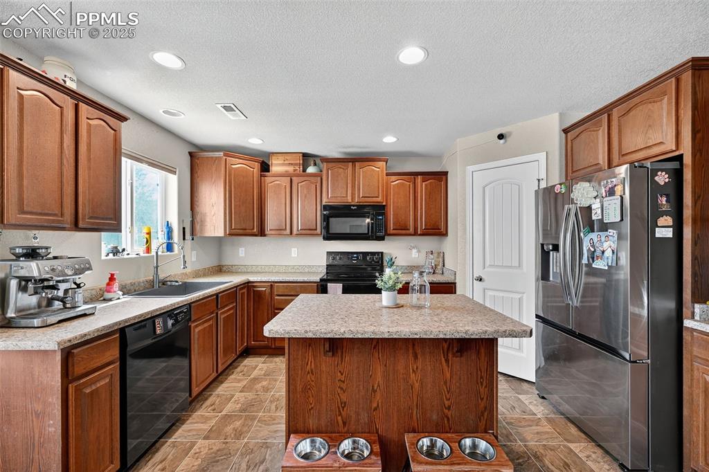 Image 11 of 33: Kitchen featuring black appliances, a center island, brown cabinets, recess