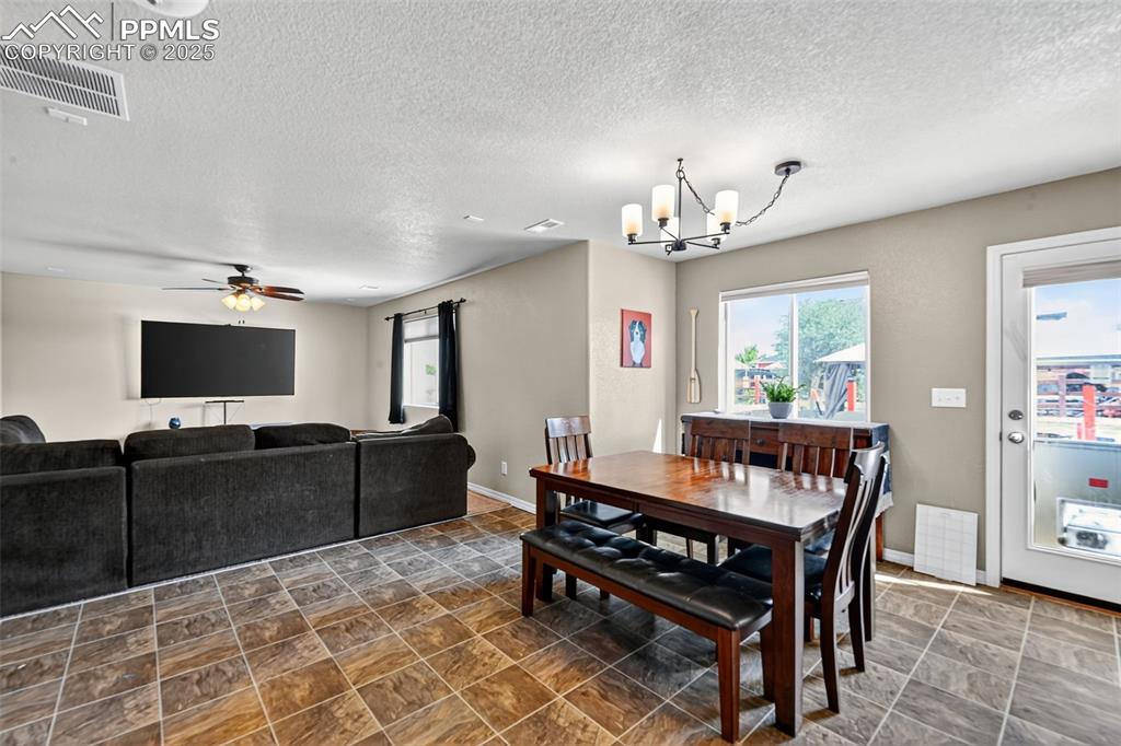 Image 13 of 33: Dining space with a textured ceiling, a chandelier, a ceiling fan, and ston