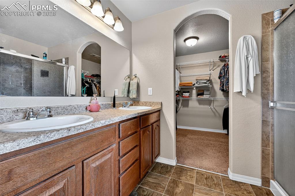 Image 23 of 33: Full bath with a walk in closet, a shower stall, and a textured wall