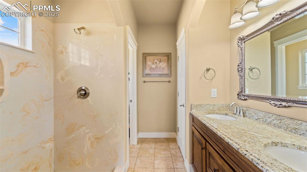 Image 20 of 50: Bathroom with double vanity, a shower, and tile patterned flooring