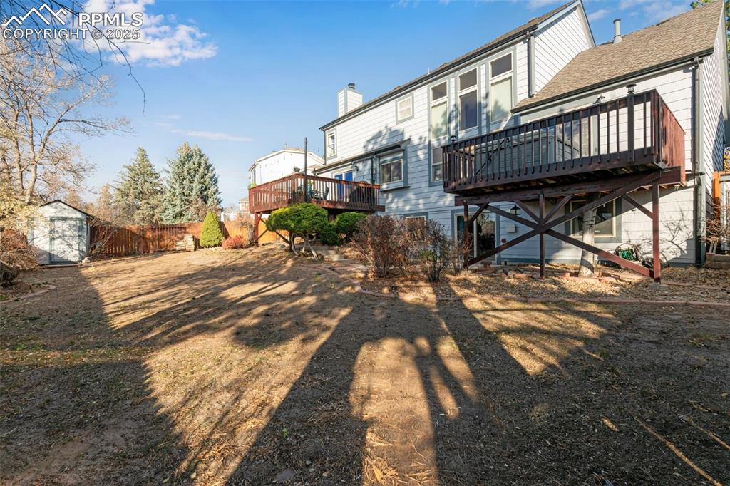 Image 29 of 41: Rear view of house with a wooden deck, a shed, a shingled roof, and a chimn