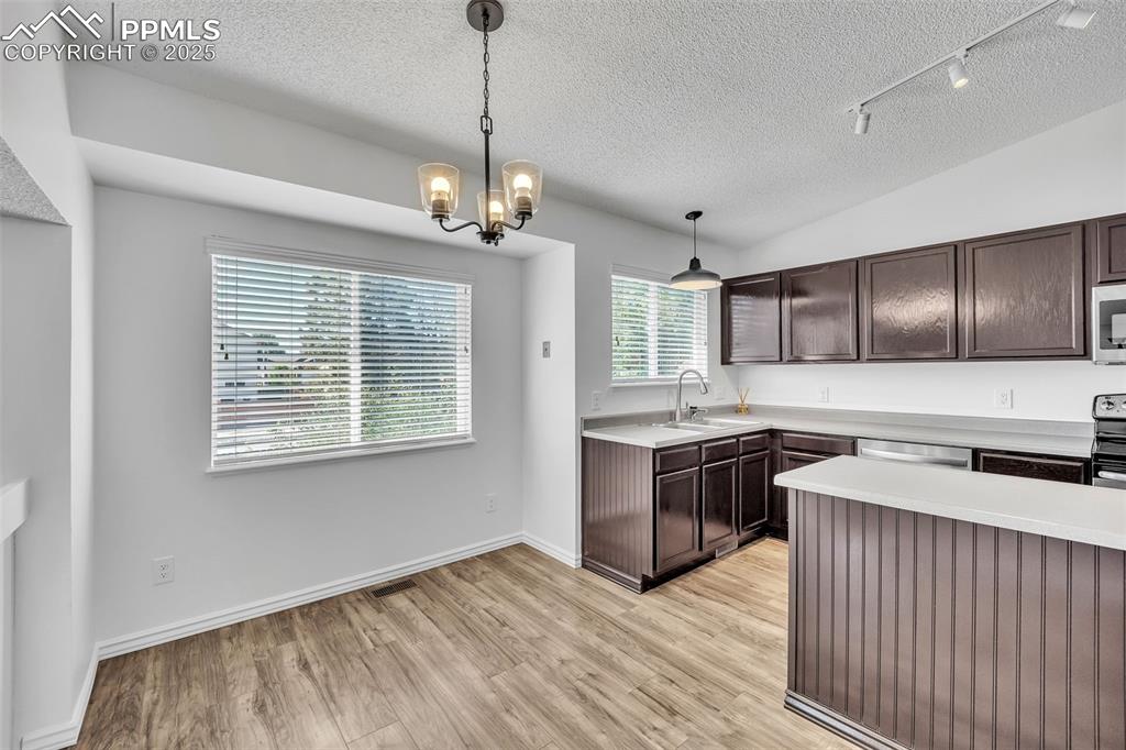 Image 11 of 43: Kitchen with dark brown cabinetry, hanging light fixtures, light countertop