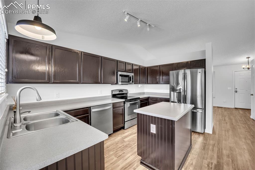 Image 2 of 43: Kitchen with hanging light fixtures, dark brown cabinetry, appliances with