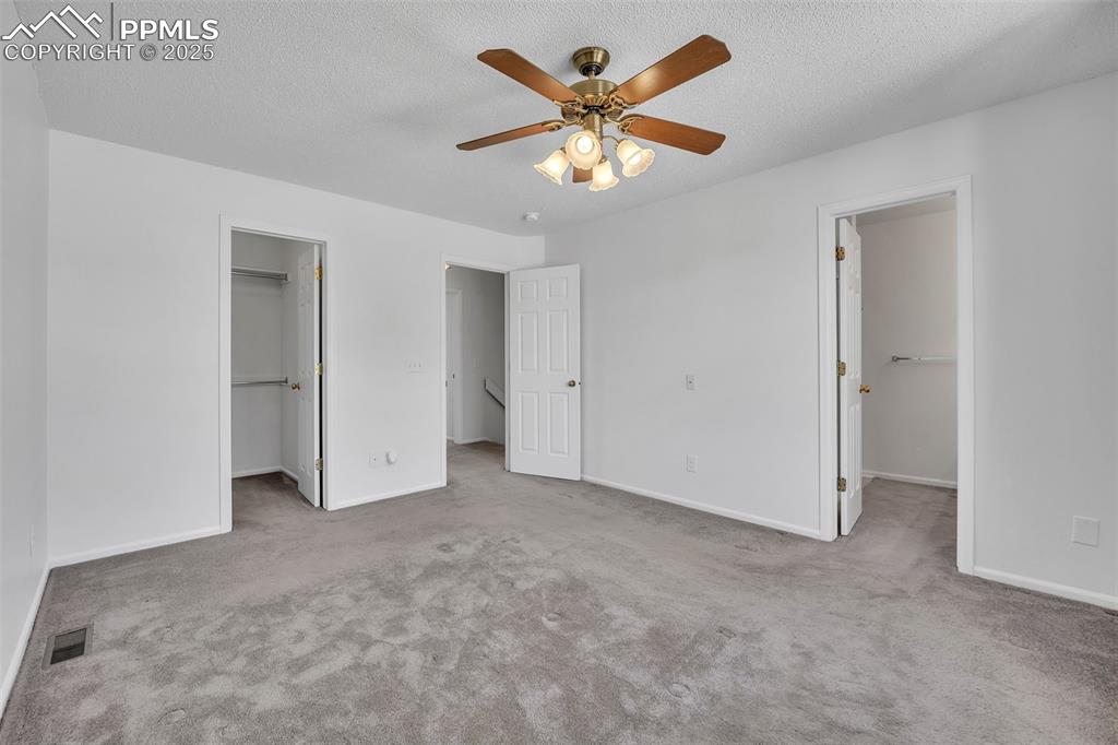 Image 27 of 43: Unfurnished bedroom featuring a walk in closet, light carpet, a textured ce