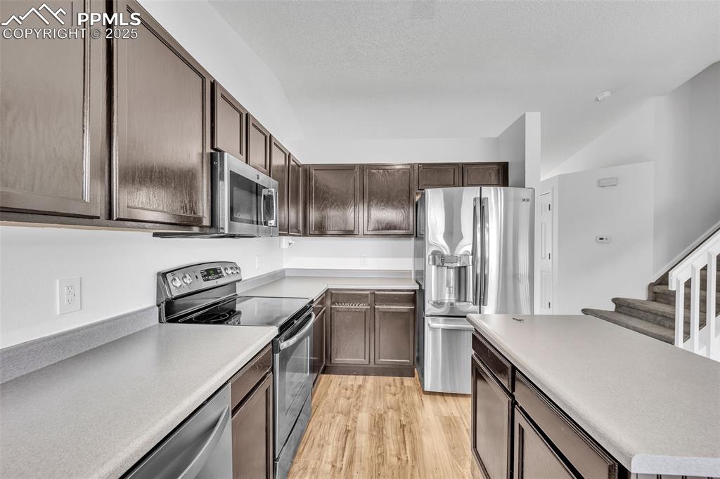 Image 9 of 43: Kitchen with stainless steel appliances, light wood-type flooring, dark bro