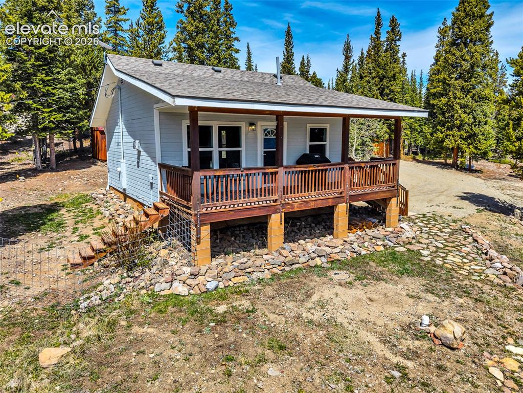 Image 2 of 37: Elevated cabin-style residence featuring light blue siding and a covered fr