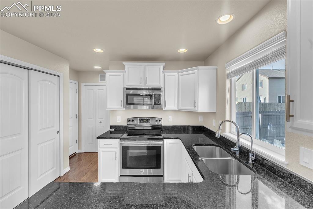 Image 11 of 28: Kitchen with stainless steel appliances, white cabinetry, dark stone counte