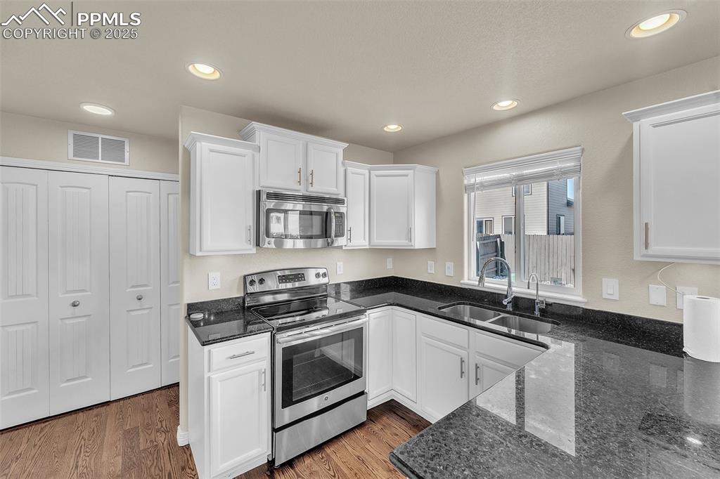 Image 12 of 28: Kitchen with stainless steel appliances, white cabinets, dark stone counter