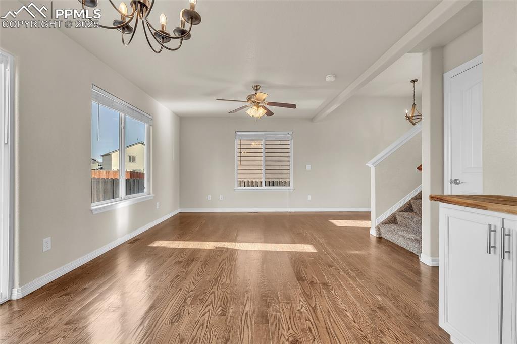 Image 8 of 28: Unfurnished living room featuring wood finished floors, stairs, a chandelie