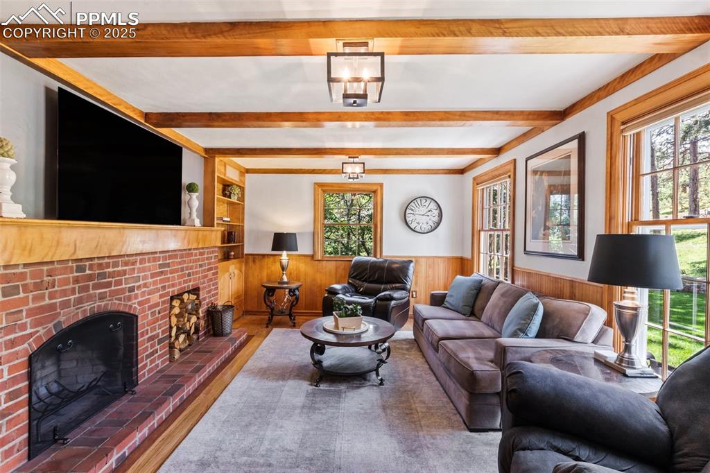 Image 15 of 50: Living area featuring beamed ceiling, a wainscoted walls, wood burning fire
