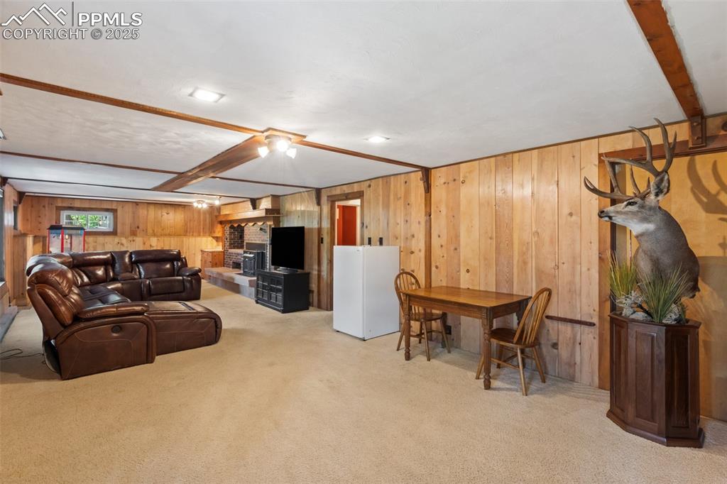Image 37 of 50: Basement living room with light colored carpet, wooden walls, a brick firep