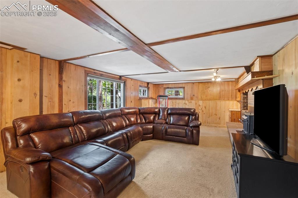 Image 38 of 50: Basement living room with wood walls, carpet, a fireplace, and beamed ceili