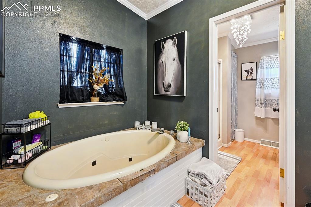 Image 43 of 48: Bathroom featuring crown molding, a bath, wood finished floors, and a textu