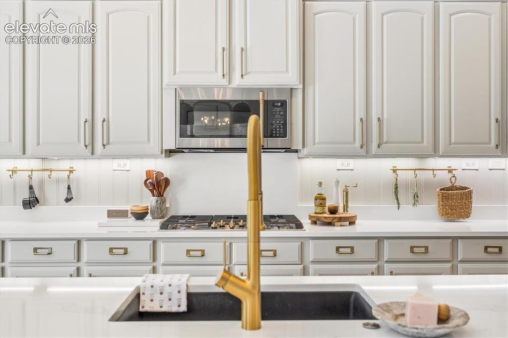 Image 13 of 50: Kitchen featuring white paneled cabinetry, stainless steel microwave, gas r