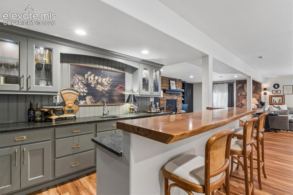 Image 34 of 50: Custom wet bar featuring a live-edge wood countertop, recessed lighting, gr