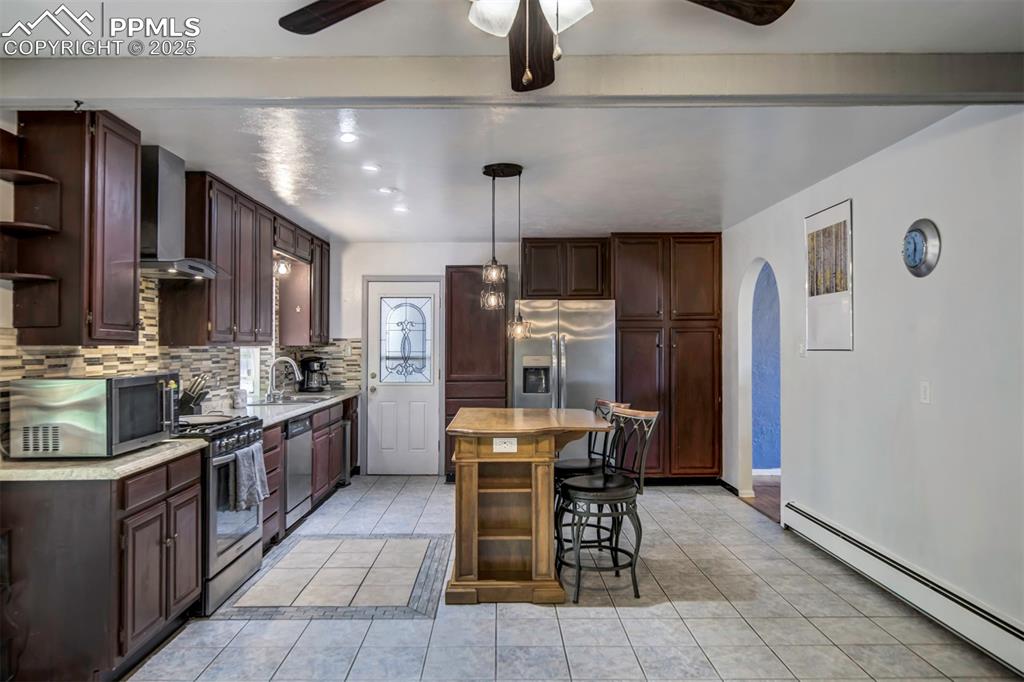 Image 14 of 44: Kitchen featuring baseboard heating, open shelves, a kitchen bar, tasteful