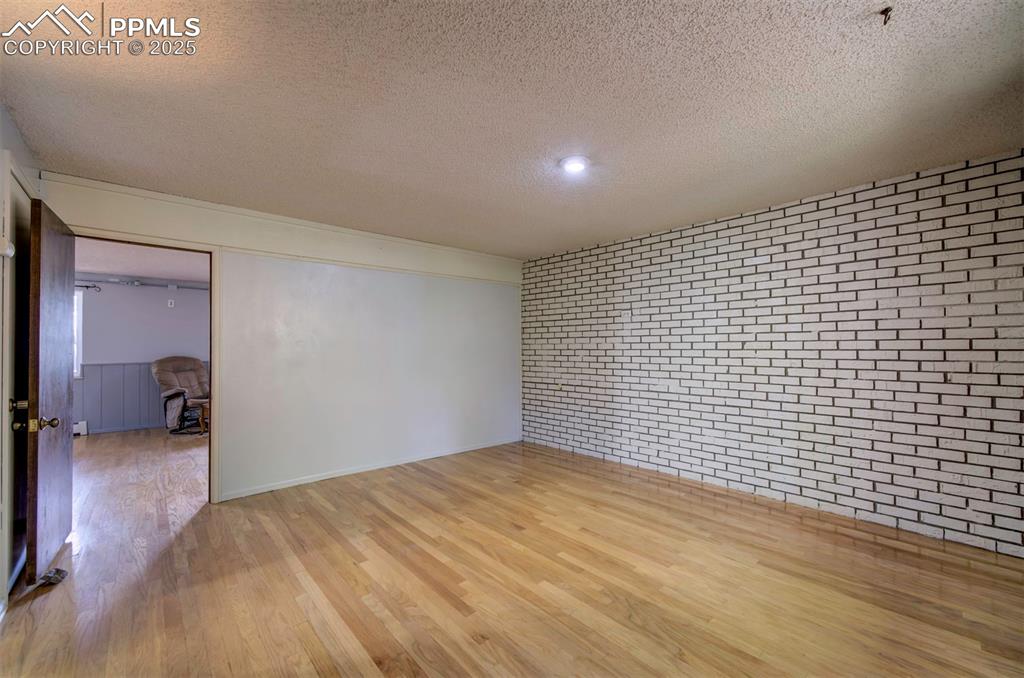 Image 21 of 44: Empty room with a textured ceiling, light wood finished floors, brick wall,
