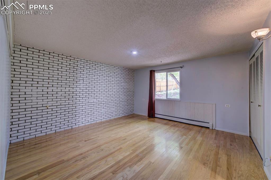 Image 22 of 44: Unfurnished room featuring brick wall, light wood-type flooring, a textured