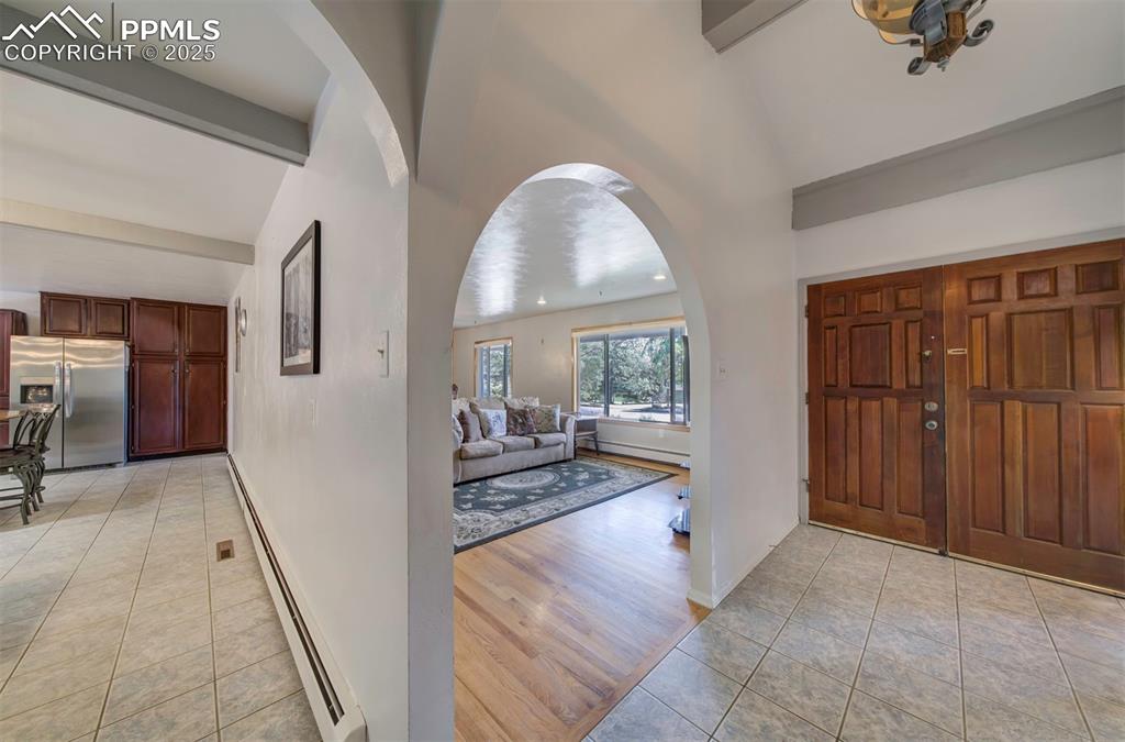 Image 5 of 44: Entryway with light tile patterned floors, a baseboard radiator, and arched