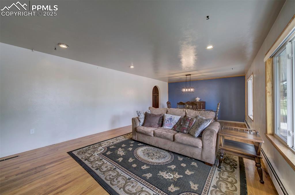 Image 8 of 44: Living area with a baseboard radiator, wood finished floors, arched walkway