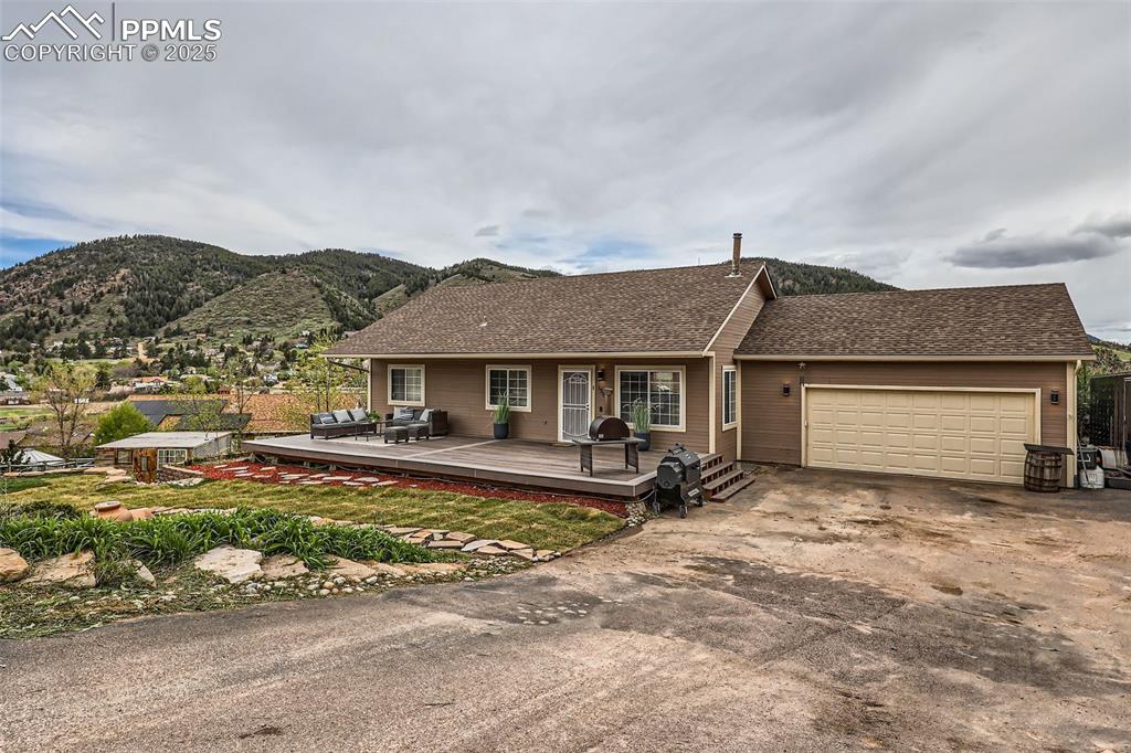 Caption: Ranch-style house featuring a shingled roof, driveway, a deck, and a garage