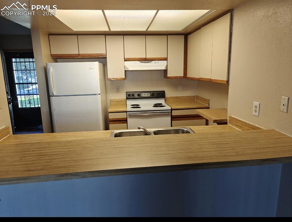 Image 7 of 17: Kitchen featuring white appliances, under cabinet range hood, a peninsula, 