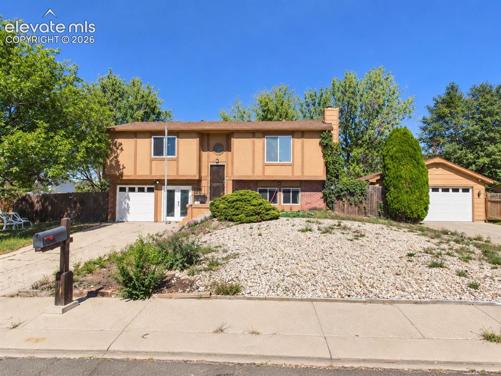 Caption: Wide front elevation showcases the bi-level home, low-maintenance rock landscaping, attached one-car