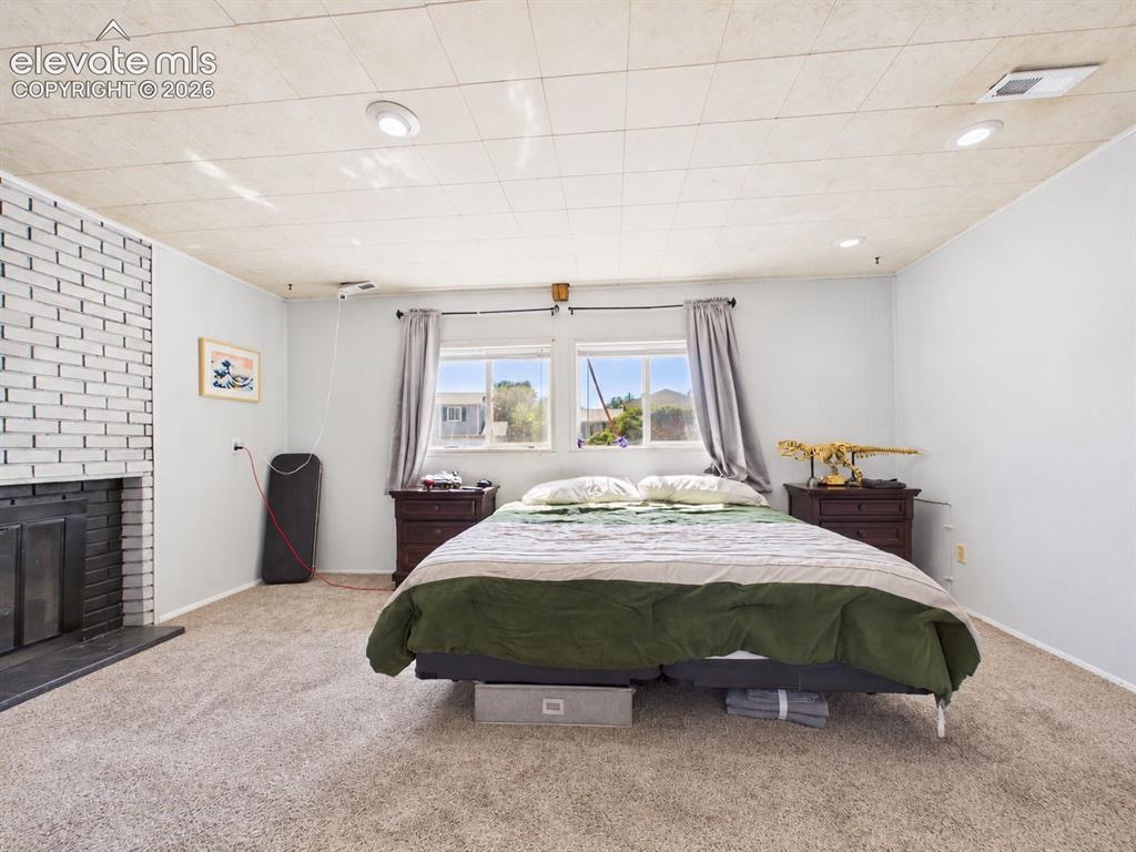 Image 30 of 50: Spacious bedroom features a distinctive painted-brick fireplace, recessed l