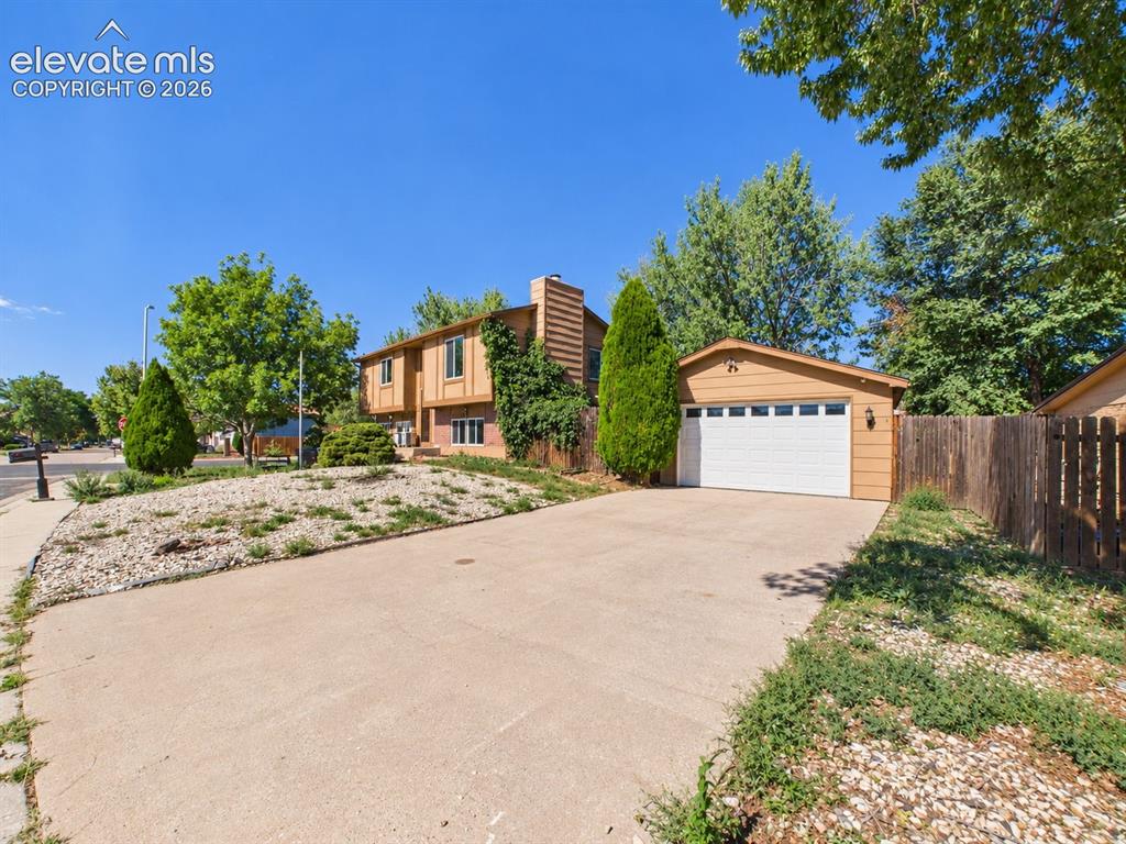 Image 43 of 50: Split-level exterior features a broad driveway, mature landscaping, and mul