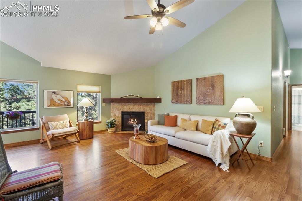 Image 11 of 43: Living area with wood finished floors, a ceiling fan, a tiled fireplace, an