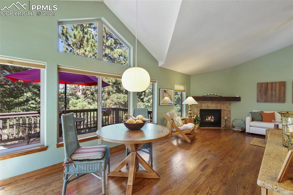 Image 14 of 43: Dining area with a fireplace, wood finished floors, and high vaulted ceilin