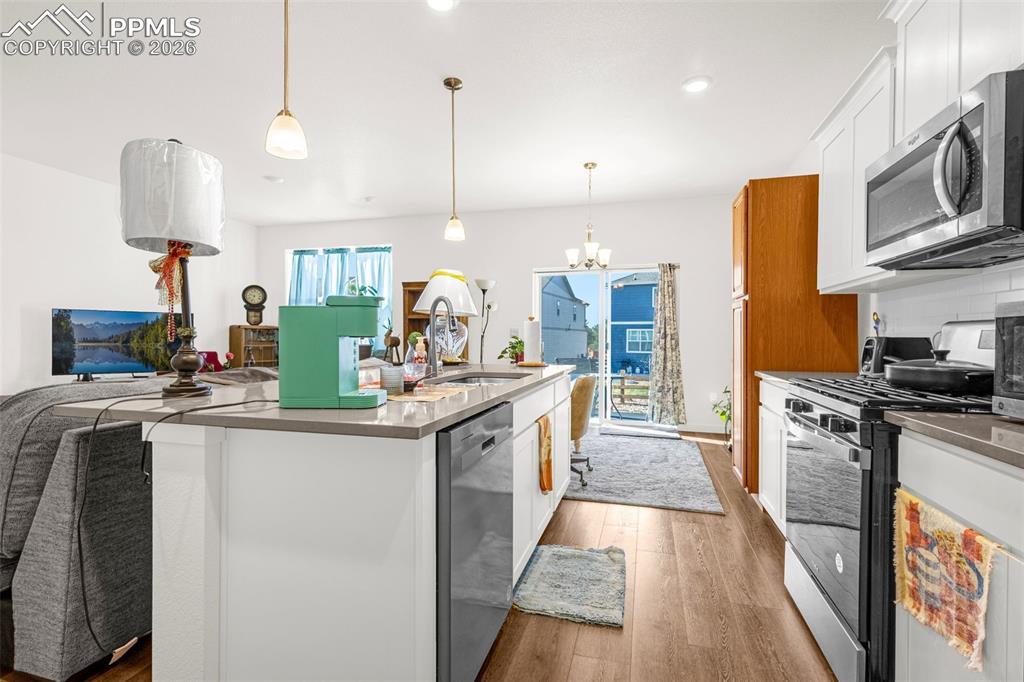 Image 7 of 27: Kitchen featuring a notable chandelier, white cabinetry, appliances with st