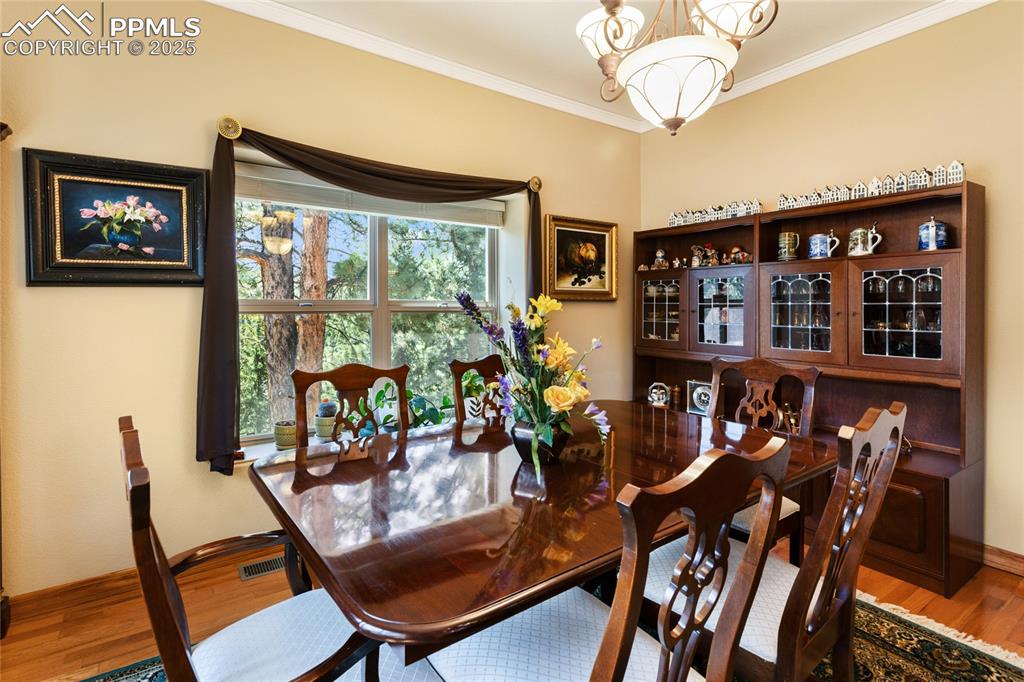 Image 15 of 47: Dining area with ornamental molding, wood finished floors, and a chandelier