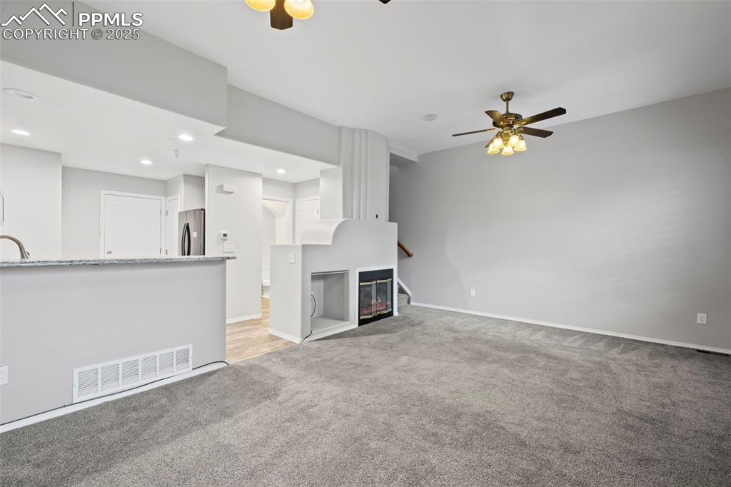 Image 11 of 23: Unfurnished living room with a ceiling fan, light colored carpet, baseboard