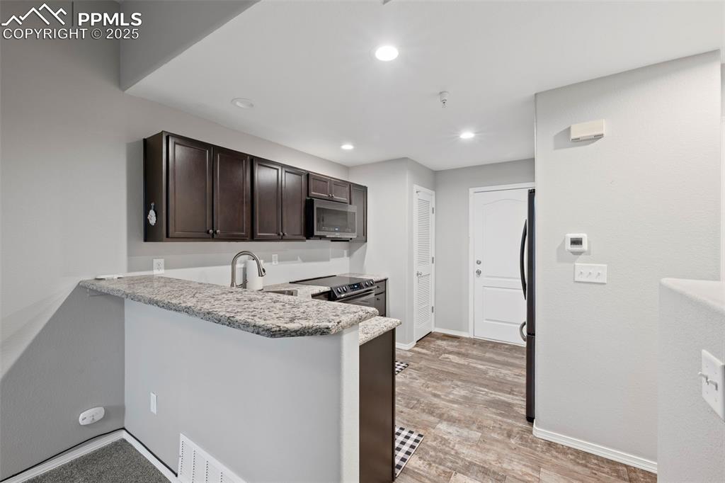 Image 12 of 23: Kitchen featuring stainless steel appliances, dark brown cabinetry, recesse