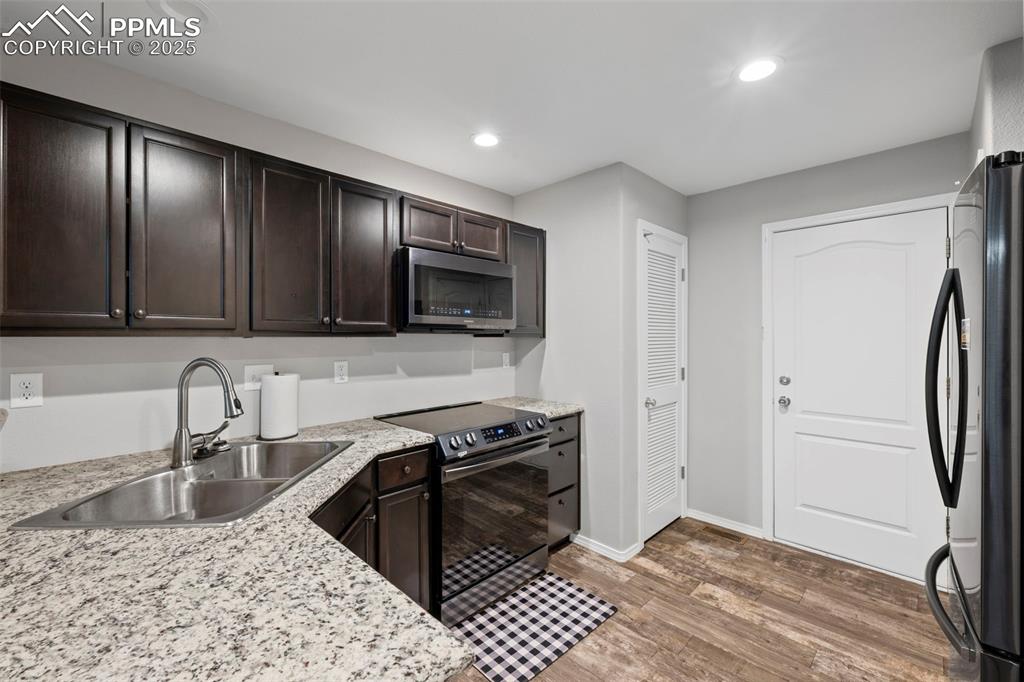 Image 13 of 23: Kitchen with black appliances, a sink, dark brown cabinetry, light wood-sty