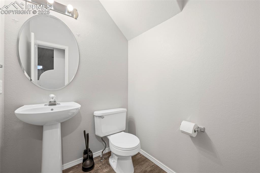 Image 15 of 23: Half bath with toilet, wood finished floors, lofted ceiling, baseboards, an