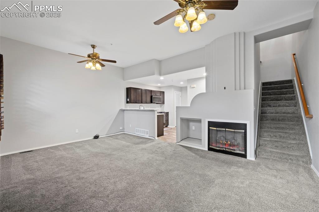 Image 9 of 23: Unfurnished living room with a ceiling fan, light carpet, baseboards, and s