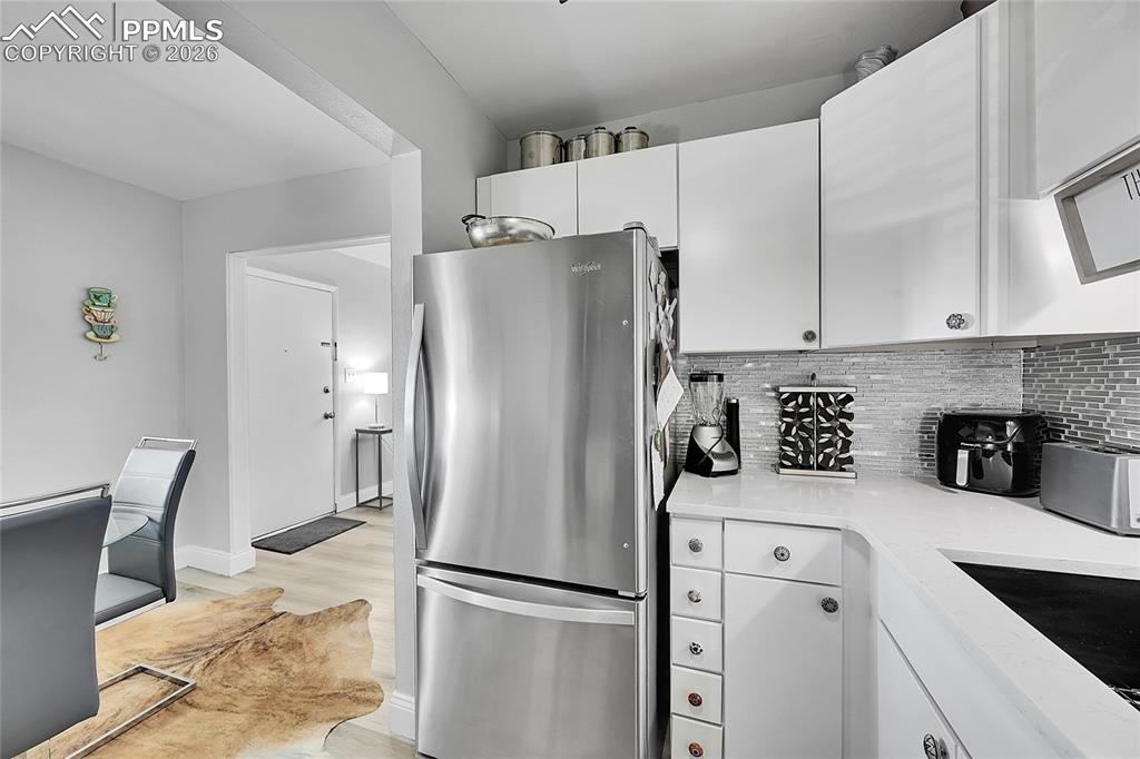 Image 9 of 42: Kitchen with sink, decorative backsplash, white cabinetry, light hardwood /