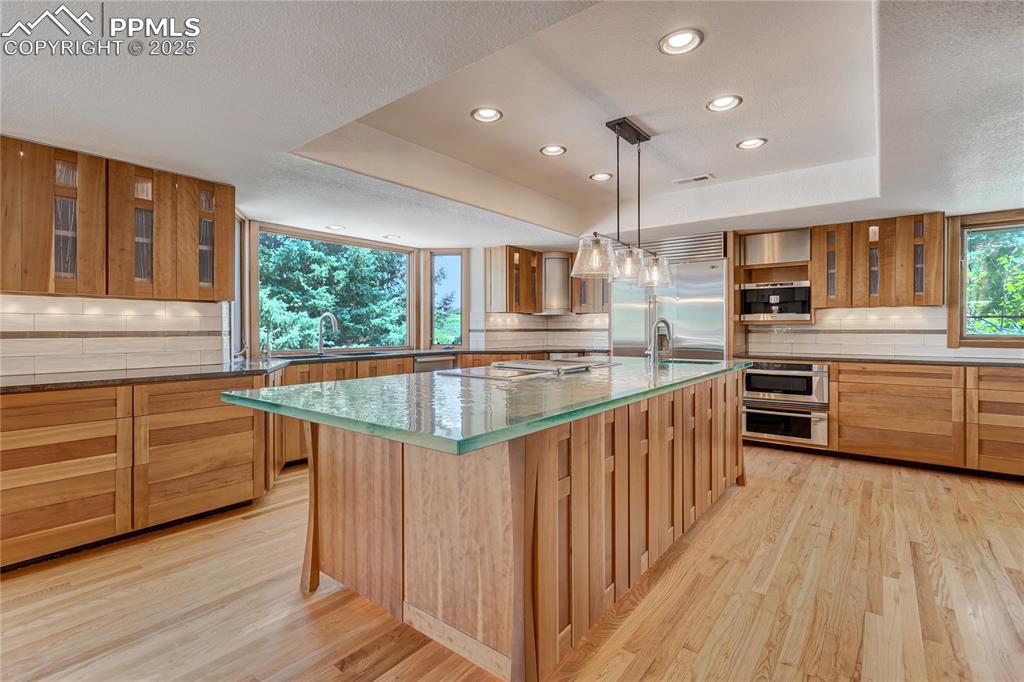 Image 11 of 50: Kitchen featuring glass insert cabinets, decorative backsplash, a tray ceil