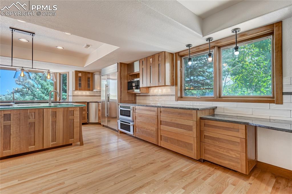 Image 13 of 50: Kitchen with decorative light fixtures, tasteful backsplash, light wood fin