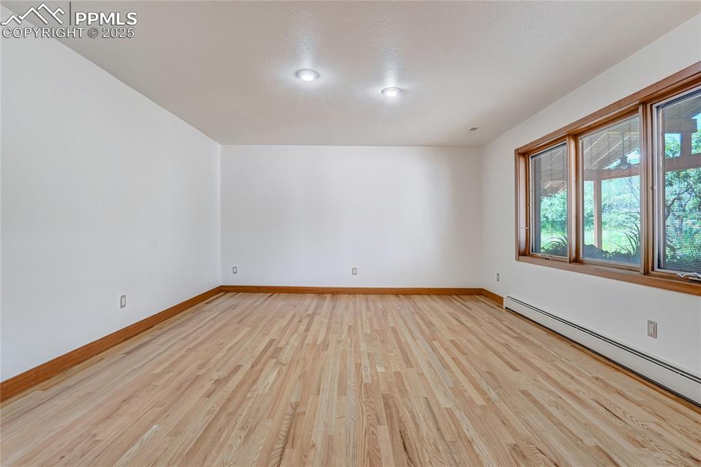 Image 44 of 50: Empty room with light wood-style flooring and a baseboard heating unit