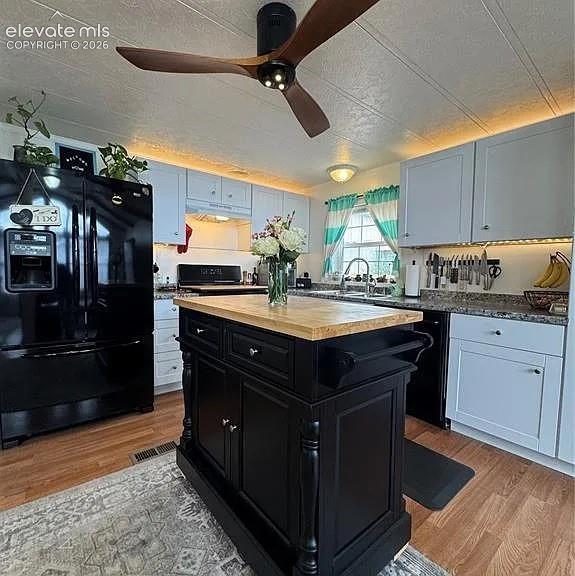 Image 10 of 34: Kitchen featuring a central island with a wood countertop, black cabinetry,