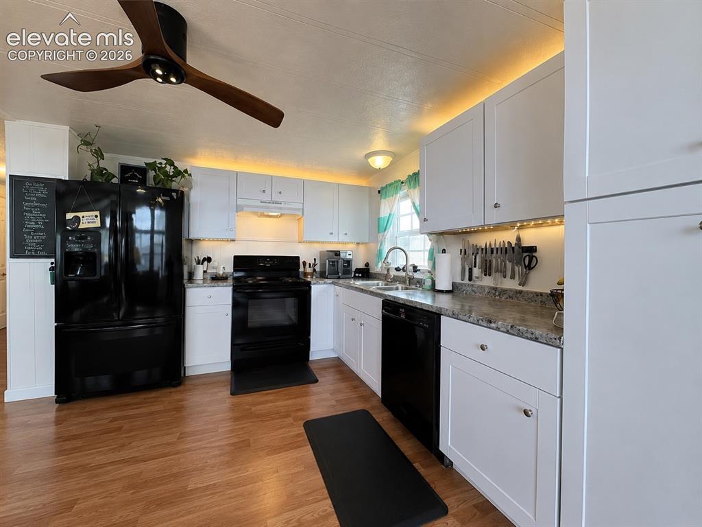 Image 12 of 34: Modern kitchen featuring crisp white cabinetry, wood-finish flooring, a bla