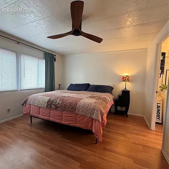 Image 23 of 34: Spacious room featuring wood-finish flooring and two windows with blinds