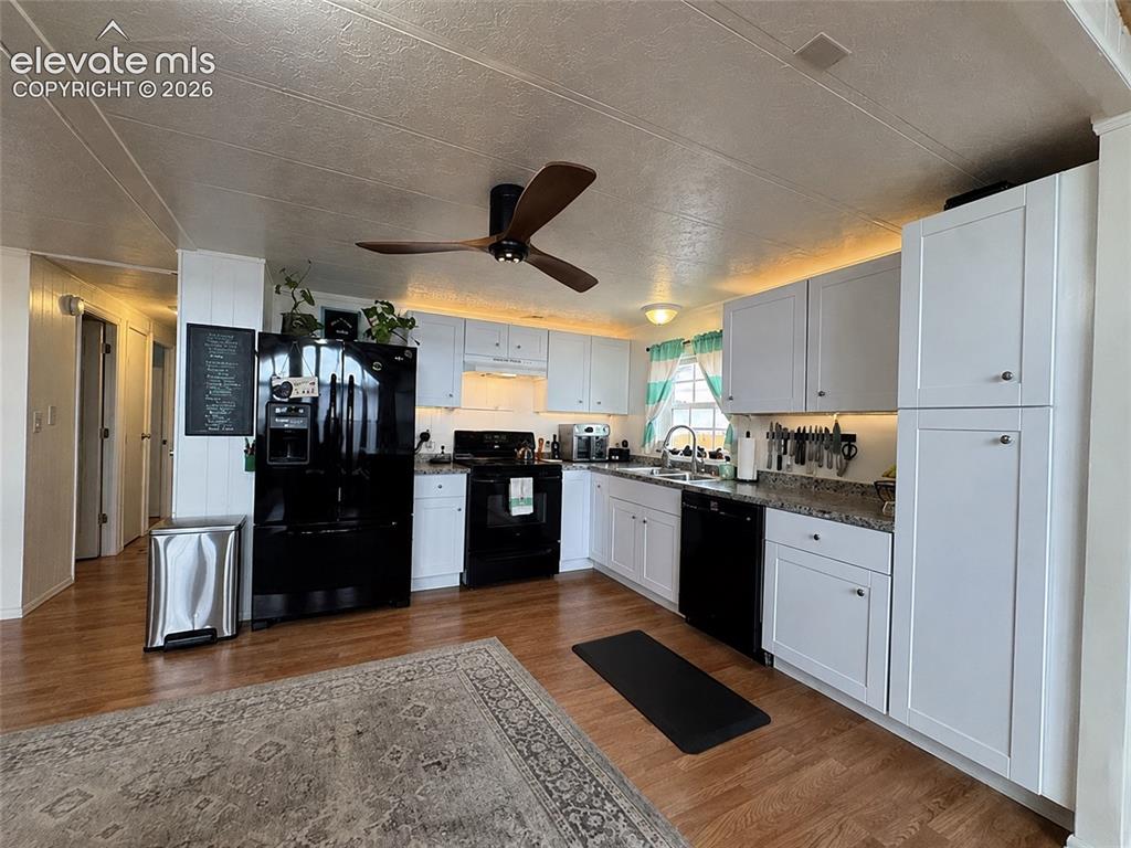 Image 8 of 34: Kitchen featuring white cabinetry, granite-patterned countertops, wood-fini